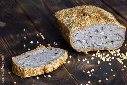 Vegan buckwheat bread. Freshly baked traditional bread on dark brown wooden table. Scattered grains and loaf near it. Selective focus. Healthy nutrition. Harmless bakery. Home-made natural food
