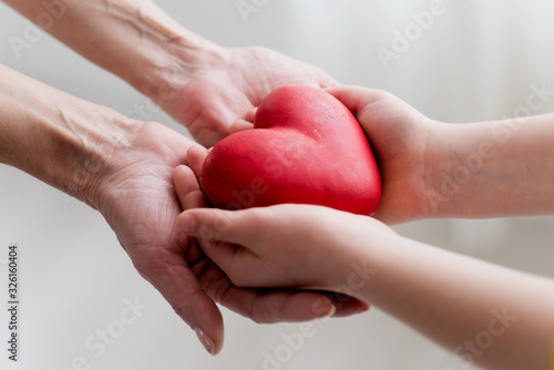 Childs hands and older woman hands holding heart. Concept o love, share and care. Care for elderly concept.
