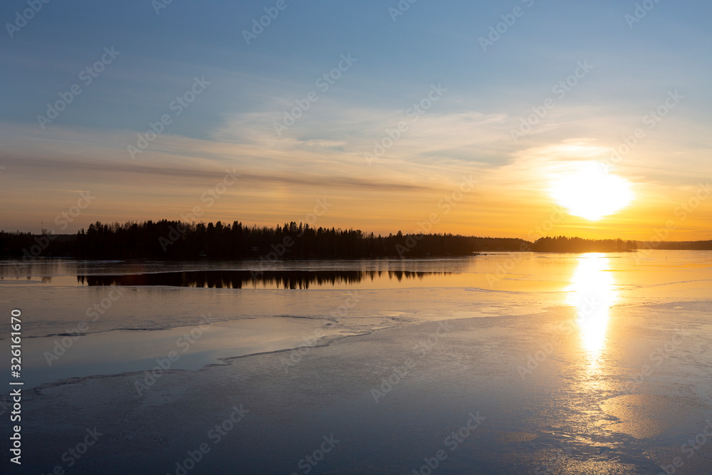 Amazing winter sunset in Finland. Cold afternoon in February, reflecting water and icy surface. Wintry landscape wallpaper, copy space.