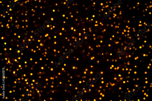 Abstract blurry golden bokeh on black background. Flickering lights pattern, festive backdrop. Concept of New Year holidays, Christmas, party. Layout for design. Sparkling magical glitter lights.