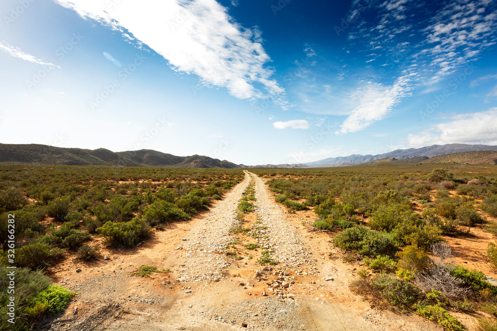 Scenic gravel road in African nature  along route 62 with gradient blue cloudy sky 