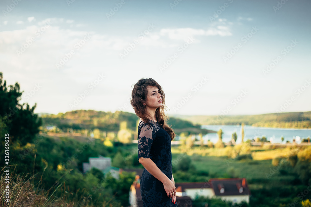 Girl in a black dress and magnificent wavy hair on the nature.