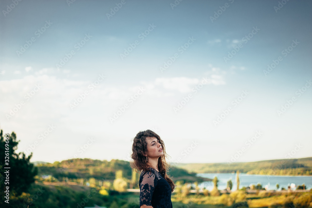 Girl in a black dress and magnificent wavy hair on the nature.