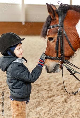 boy stroking horse, young jockey, horseback training on manege, lesson for young jockey in equestrian school or club, pet animal