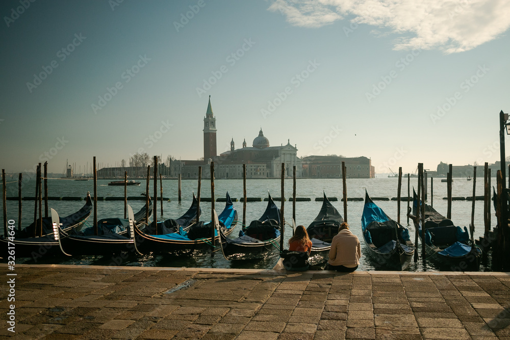 Mujeres sentadas a la orilla del mar en Venecia frene a las góndolas