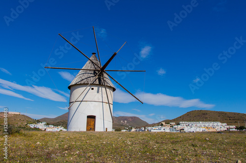 traditional windmill and behind the village of El Pozo de los Frailes, windmill traditional in Spain, Pozo de los Frailes, province of Almeria, windmill under blue sky