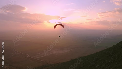 Lonely silhouette of pilot fly on parachute in sunset. Beautiful epic pink sunset over mountains. Professional paraglider enjoys fresh air and extreme adrenaline while in air photo