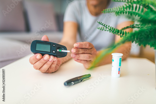Tapet Close up of woman hands using lancet on finger to check blood sugar level by Glu