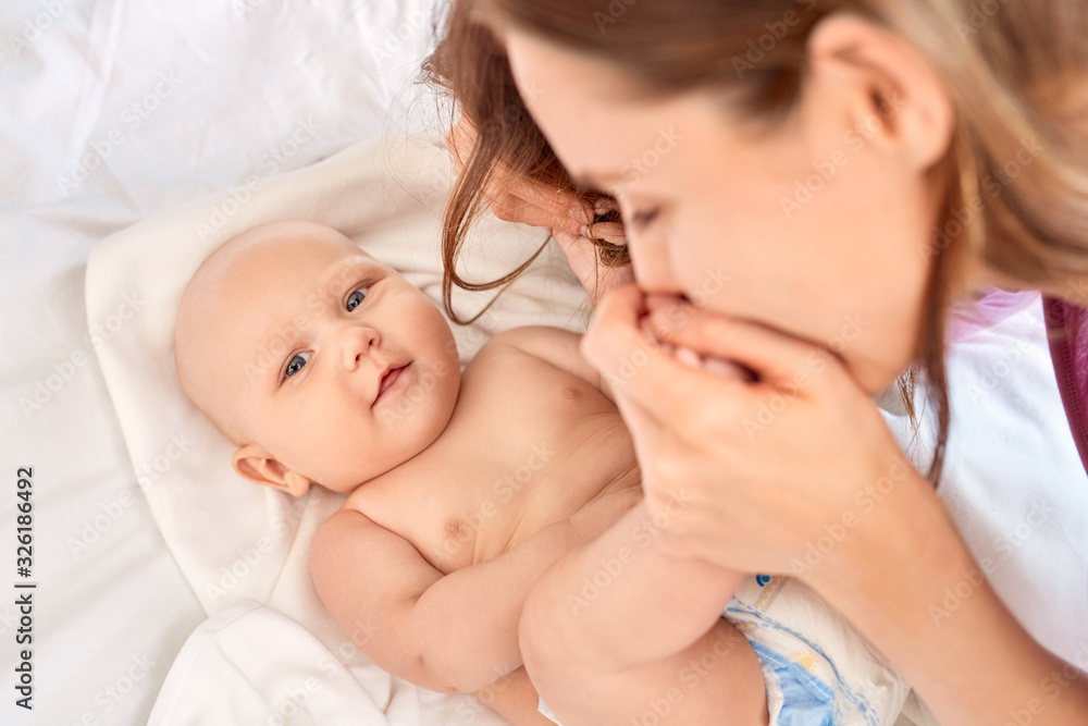 Young adult mother kissing feet her little new born baby Young adult mother kissing feet her little new born baby