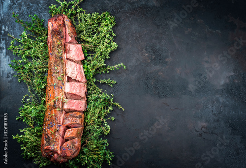 Barbecued dry aged venison tenderloin fillet steak and saddle natural with herbs offered as top view on a rustic board with copy space right photo