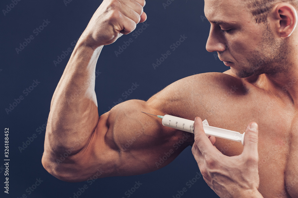 Bodybuilder makes injection of vitamins. Photo of sporty man with perfect physique on dark