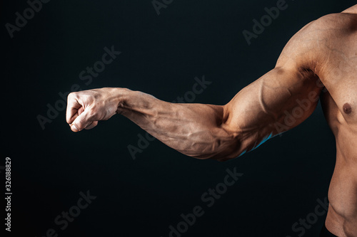 tense arm clenched into fist, veins, bodybuilder muscles on a dark background, isolate. photo