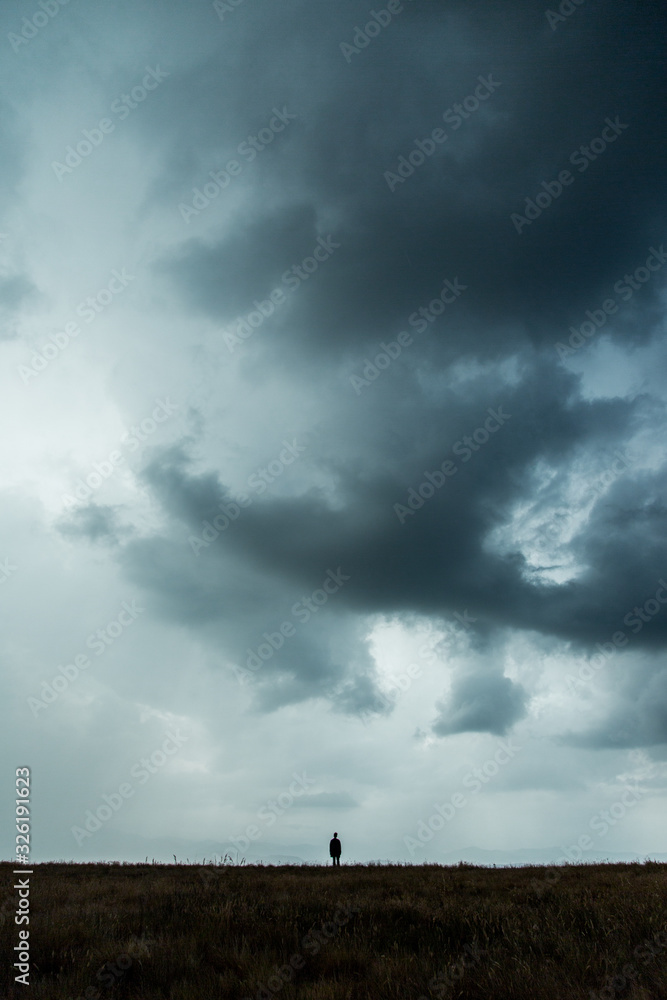 Person stands storm clouds over field