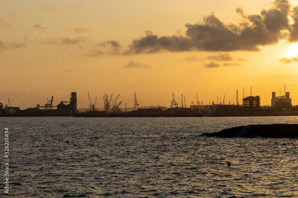 sunset over city with buildings growing, sea shore and building cranes