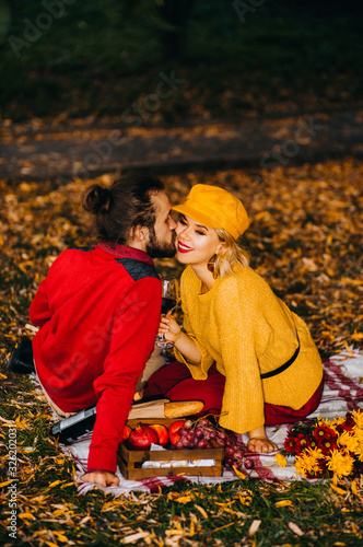 A guy with a ponytail kisses his girlfriend in a yellow sweater during a picnic in the park.