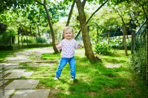 Adorable baby girl walking in green park on a summer day
