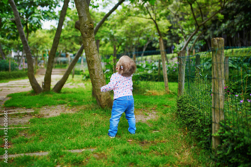 Adorable baby girl walking in green park on a summer day