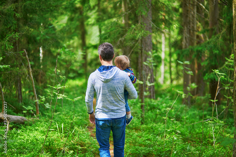 Father carrying his child during walk in forest - obrazy, fototapety, plakaty 