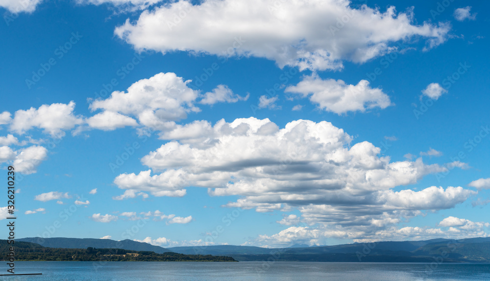 Panoramic photo of a group of white clouds between a blue sky and a lake in southern Chile