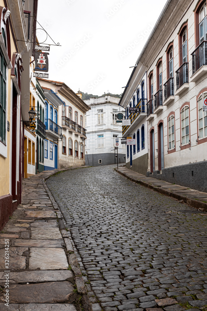Fototapeta premium Vertical steep wet cobblestone street leading to white corner building passing the typical historic colonial colourful exterior facade architecture