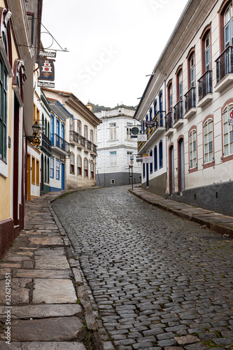 Fototapeta Naklejka Na Ścianę i Meble -  Vertical steep wet cobblestone street leading to white corner building passing the typical historic colonial colourful exterior facade architecture