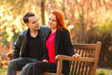 A young man and a girl are sitting on a wooden bench