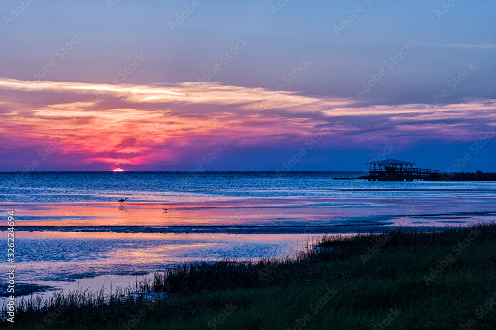 Sunset on Florida beach with water birds and a dock with gazebo in the distance