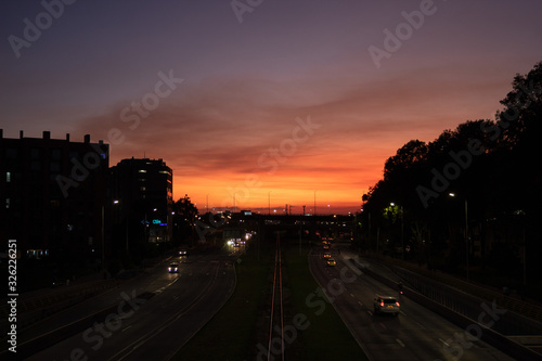 100th street with 9th avenue in a beautiful color sunset with cars lights and railroad in middle of capture.