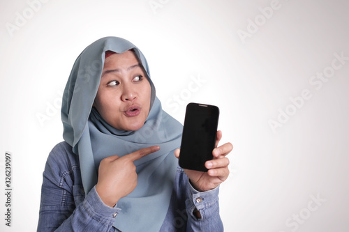 Muslim Woman Holding Phone and Pointing Side, Presenting Something © airdone