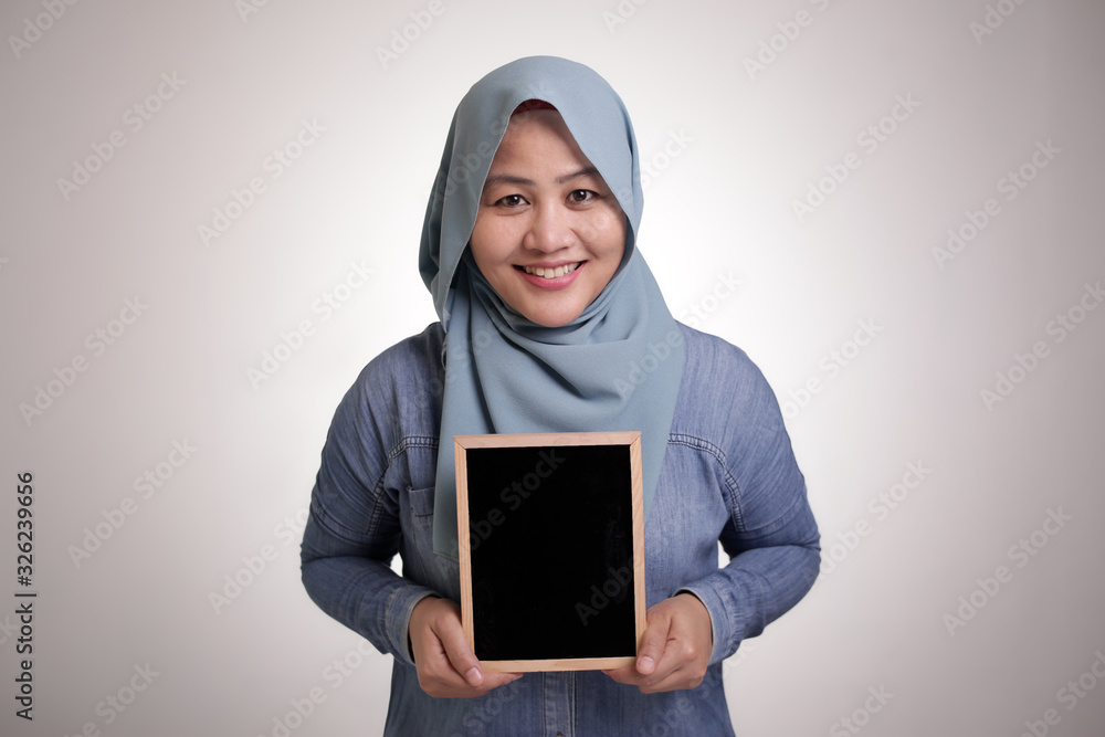 Smart Asian Muslim Woman Smiling at Camera and Showing Empty Blackboard Smart Asian Muslim Woman Smiling at Camera and Showing Empty Blackboard