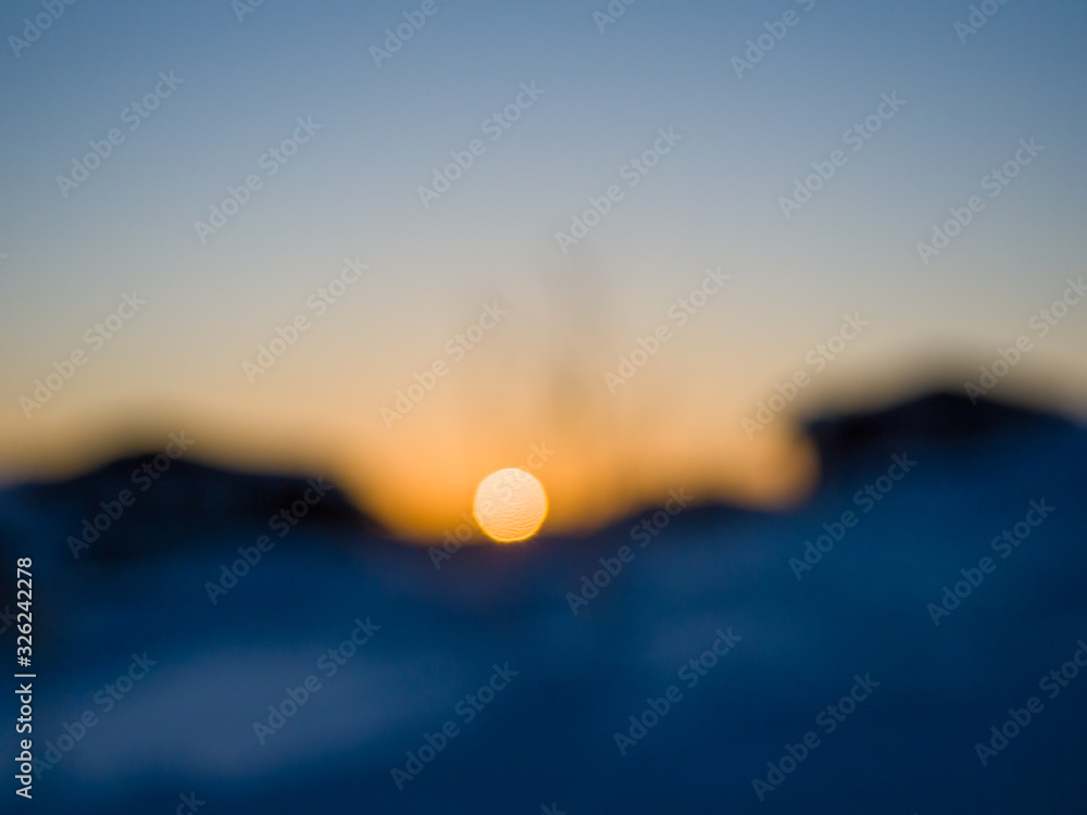 Plakat Defocused sunrise. The sun appears over the horizon between wooden houses. Winter morning in Siberia