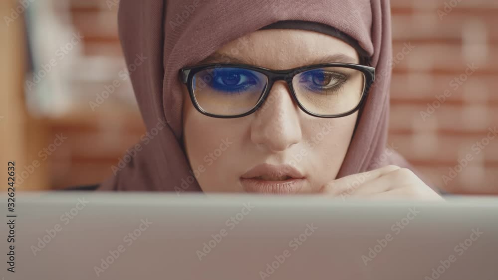 A Muslim woman looks at the laptop screen, the view from the back of the laptop. A girl in a hijab is working on a laptop A Muslim woman looks at the laptop screen, the view from the back of the laptop. A girl in a hijab is working on a laptop