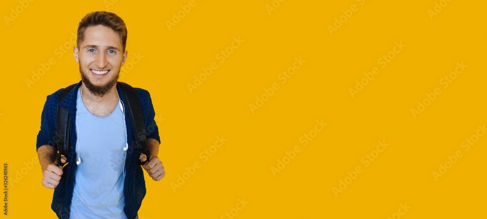 Ginger caucasian student posing with a bag on his shoulders while smiling aside on a yellow wall with freespace Ginger caucasian student posing with a bag on his shoulders while smiling aside on a yellow wall with freespace