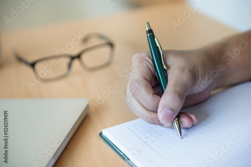 The hand of a businessman who holds a pen to write on the desk. Select focus on hand.