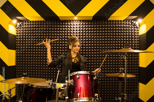 young beautiful tattooed girl in a leather jacket plays drums in a recording Studio on the bright black and yellow band