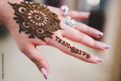 Close up of 'Team Bride' written on a girl's hand with Mehendi tattoo artwork. Mandala pattern green Henna art on a bridesmaid hand at a Mehndi ceremony. Isolated hand with blurred background. photo
