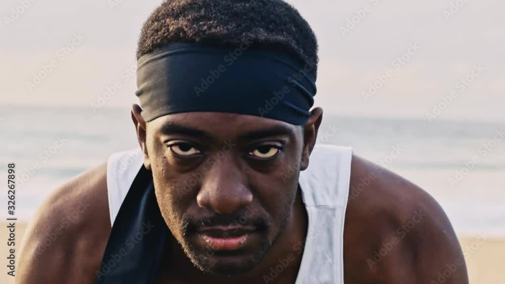 Dramatic close-up of a black athlete doing pushups on the beach whilst staring intently at the camera. Dramatic close-up of a black athlete doing pushups on the beach whilst staring intently at the camera.