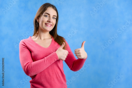 Portrait on a blue background of a pretty brunette Caucasian woman in a red sweater showing hands with a smile