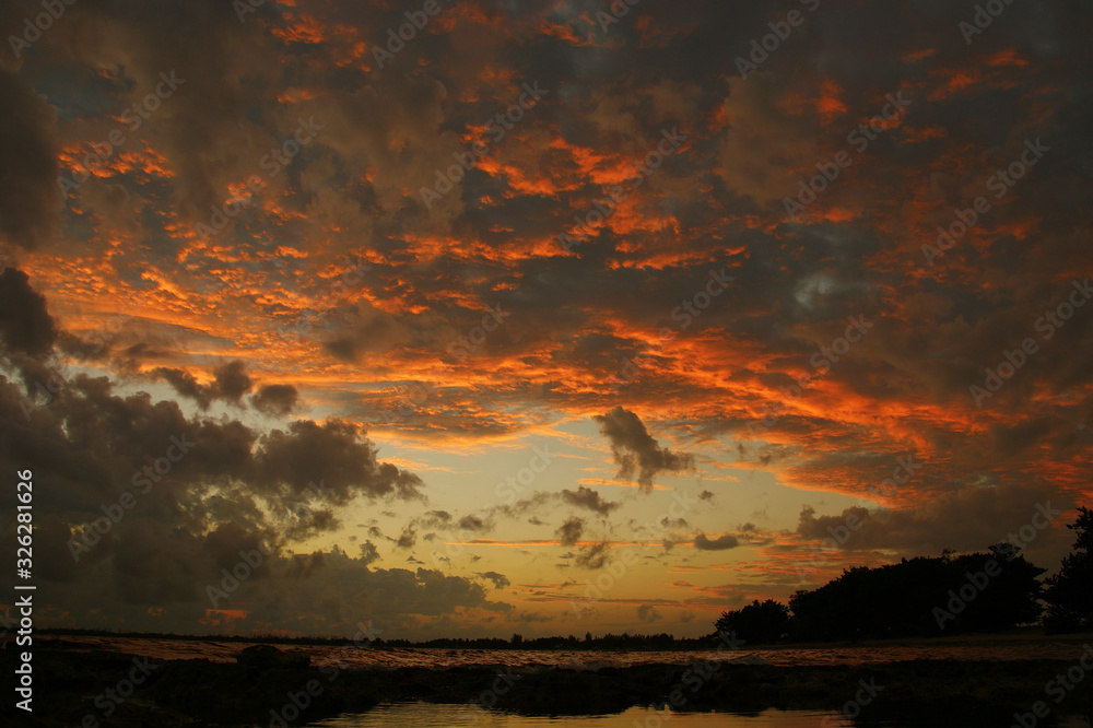 Dramatic sky at sunset with red, yellow and orange colors. The reflection of dramatic clouds in the sea enhances the effect