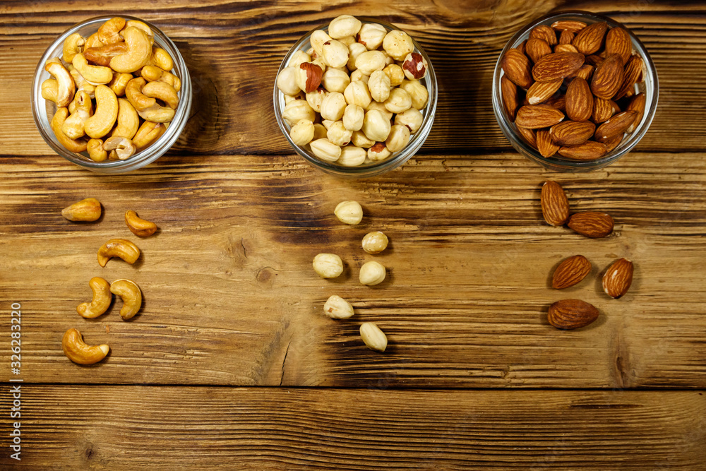 Assortment of nuts on wooden table. Almond, hazelnut and cashew in glass bowls. Top view. Healthy eating concept Assortment of nuts on wooden table. Almond, hazelnut and cashew in glass bowls. Top view. Healthy eating concept