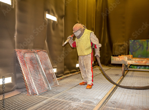 Fotografija the worker processes the sandblast in the chamber dirty part before painting