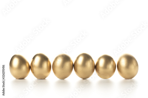 eggs painted with gold paint stand in a row on a white background. place for text on top.