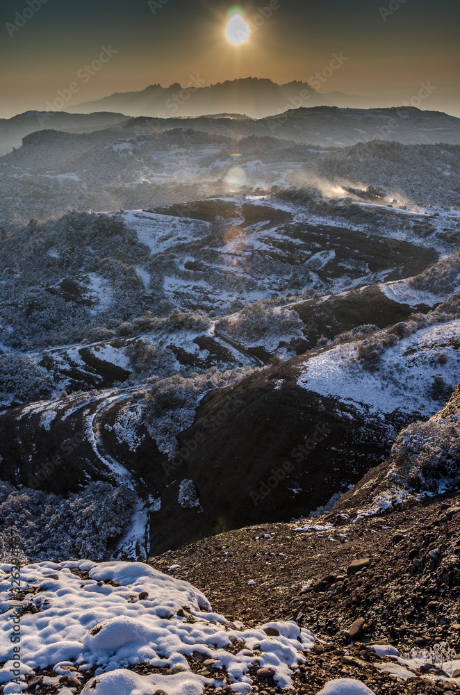 Obraz premium Paisaje nevado del parque natural de Sant Llorenç del Munt con la montaña de Montserrat al fondo al atardecer (Cataluña, España)