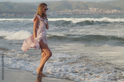 Young girl on the sea beach in a dress, evening wave and wind light, joyful mood.