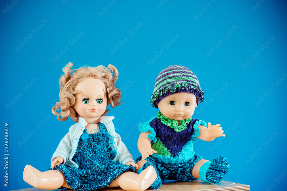 Old-Fashioned baby Doll dressed in knitted costume sits on shelf on blue background Old-Fashioned baby Doll dressed in knitted costume sits on shelf on blue background