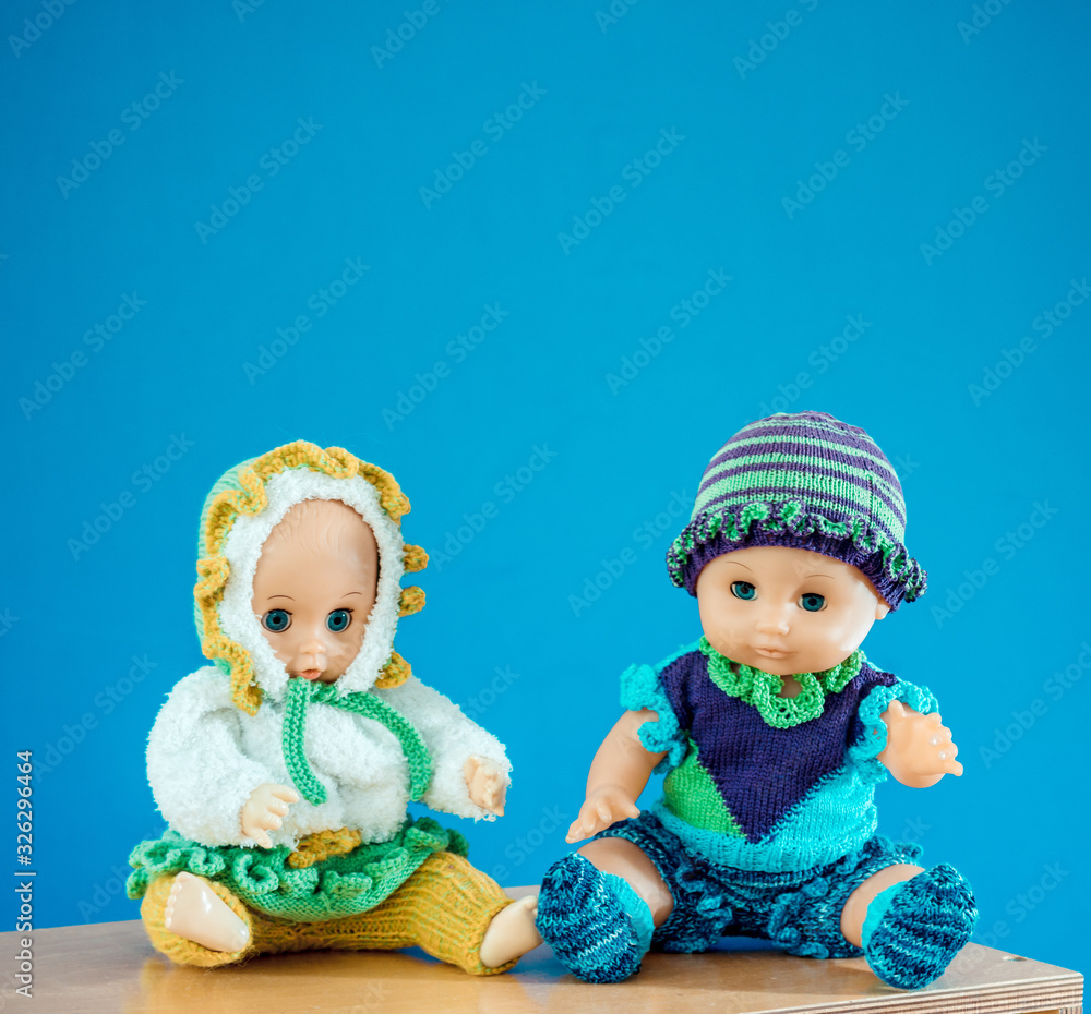 Old-Fashioned baby Doll dressed in knitted costume sits on shelf on blue background Old-Fashioned baby Doll dressed in knitted costume sits on shelf on blue background