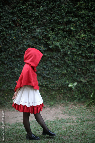 Portrait young woman with Little Red Riding Hood costume with apple and bread on basket in green tree park background