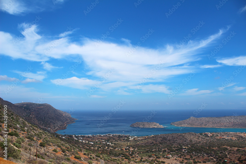 The sea coast, among the mountains of a small town. Islands along the coast against a blue sky with clouds.