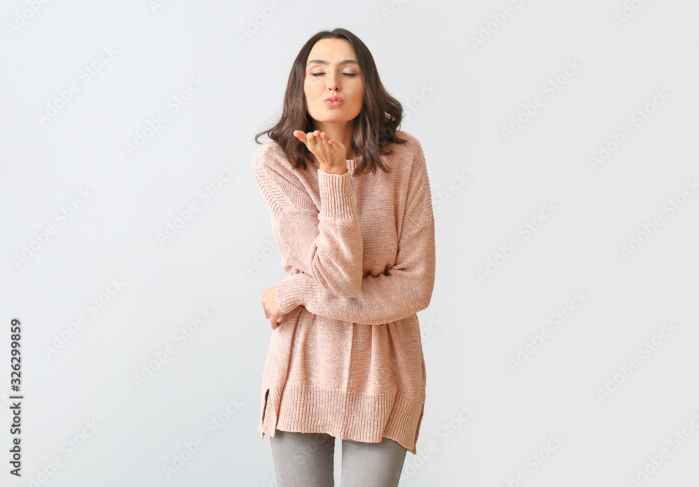 Beautiful young woman in warm sweater blowing kiss on light background Beautiful young woman in warm sweater blowing kiss on light background