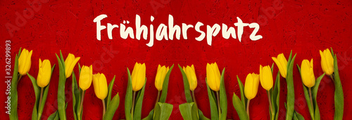 Red Wooden Background With German Text Fruehjahrsputz Means Spring Cleaning. Banner Of Yellow Tulip Flowers In Spring Season photo